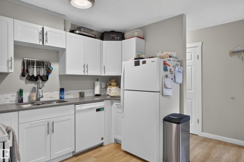 Kitchen featuring white cabinetry, a double basin sink, white appliances, light wood-finish flooring, and a patterned backsplash - 18319 93 Avenue Nw, Edmonton, AB 