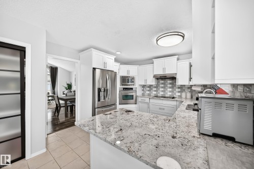Kitchen featuring white cabinetry, stainless steel appliances, granite countertops, and a tiled backsplash - 4216 47 Street Nw, Edmonton, AB 