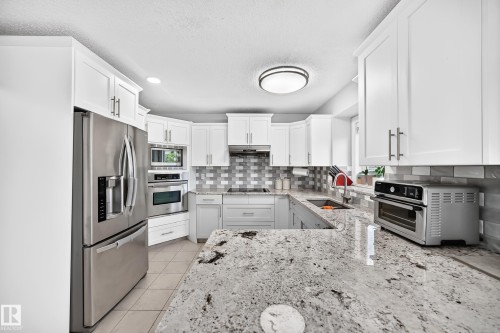 White shaker-style cabinetry, stainless steel appliances, granite countertops, tile flooring, and a subway tile backsplash - 4216 47 Street Nw, Edmonton, AB 