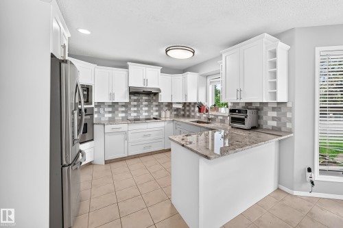 White shaker cabinetry, light-toned tile flooring, stainless steel appliances, granite countertops, and a gray subway tile backsplash - 4216 47 Street Nw, Edmonton, AB 