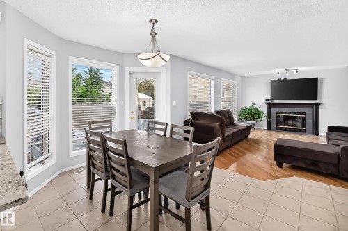 Tiled flooring in the dining area, large windows, ceiling-mounted light fixture, fireplace with a dark tile surround, and wood-finish flooring in the adjacent living area - 4216 47 Street Nw, Edmonton, AB 