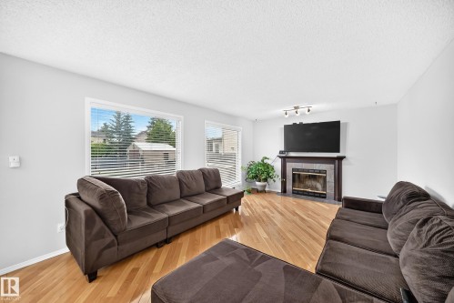 Bright living area featuring wood-finish flooring, multiple windows, a track lighting fixture, and a fireplace with a tile surround and wood mantel - 4216 47 Street Nw, Edmonton, AB 