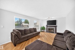 Bright living area featuring wood-finish flooring, multiple windows, a track lighting fixture, and a fireplace with a tile surround and wood mantel - 