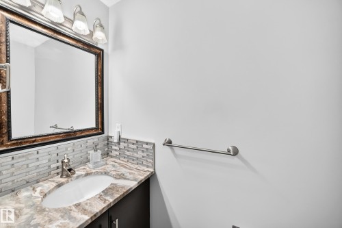 Single vanity with an oval undermount sink, multi-tone tile backsplash, patterned countertop, and dark wood-finish cabinetry - 4216 47 Street Nw, Edmonton, AB 