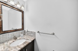 Single vanity with an oval undermount sink, multi-tone tile backsplash, patterned countertop, and dark wood-finish cabinetry - 