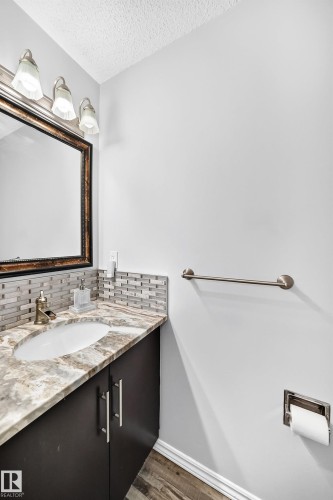 Vanity with an integrated sink, stone countertop, tile backsplash, wood-finish flooring, and a framed mirror - 4216 47 Street Nw, Edmonton, AB 