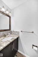 Vanity with an integrated sink, stone countertop, tile backsplash, wood-finish flooring, and a framed mirror - 