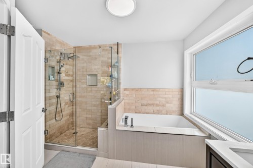 Glass-enclosed shower with stone tile surround, built-in recessed shelving, and a separate built-in bathtub - 4216 47 Street Nw, Edmonton, AB 