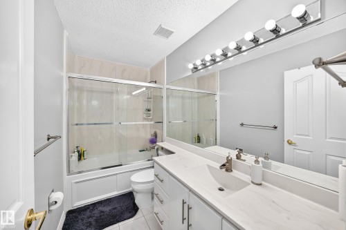 Full-length vanity mirror with overhead lighting, white double-sink vanity, and shower-tub combination with sliding glass doors - 4216 47 Street Nw, Edmonton, AB 