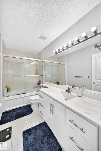 White vanity with an integrated sink and brushed nickel hardware, expansive vanity mirror, and a tub with a sliding glass enclosure - 4216 47 Street Nw, Edmonton, AB 