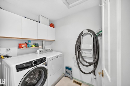 Integrated laundry space with built-in overhead cabinetry, an open shelf, and white walls - 4216 47 Street Nw, Edmonton, AB 