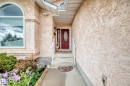 Entryway featuring stucco exterior, arched window, red door with oval glass insert, and white railing - 4216 47 Street Nw, Edmonton, AB 
