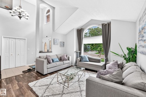 Vaulted ceiling with an elegant chandelier, wood-finish flooring, arched transom window, and a large arched window with blinds - 4216 47 Street Nw, Edmonton, AB 