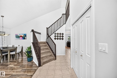 Vaulted ceiling, two-story staircase with dark wood-finish railings, tile flooring, wood-finish plank flooring, and a bifold door closet - 4216 47 Street Nw, Edmonton, AB 