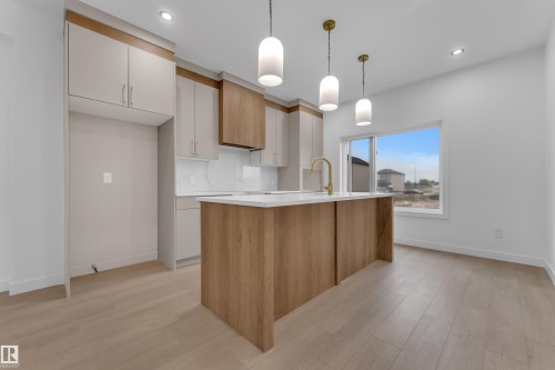 Open-concept kitchen featuring an island with a white countertop, two-tone cabinetry, and wood-finish flooring - 265 Falcon Crescent, Leduc, AB 