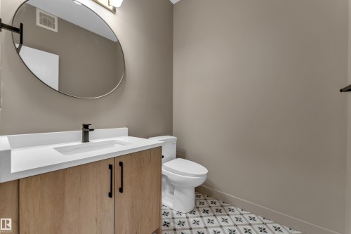 Powder room featuring a wood-finish vanity with an integrated sink, matte black faucet, and an oval-shaped mirror - 265 Falcon Crescent, Leduc, AB 