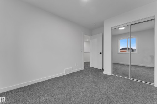 Plush gray carpeting with white baseboards, a white interior door with black hardware, and mirrored closet doors - 265 Falcon Crescent, Leduc, AB 