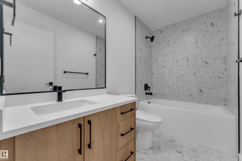 Light wood-finish vanity with matte black hardware, white countertop with integrated rectangular sink, large framed mirror, and a built-in bathtub with tiled surround - 265 Falcon Crescent, Leduc, AB 