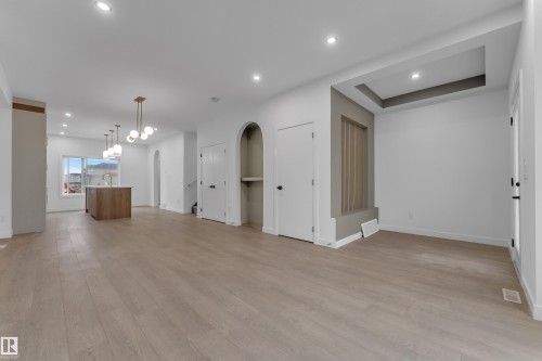 Spacious open-concept room featuring wood-finish flooring, recessed lighting, and a contemporary light fixture - 265 Falcon Crescent, Leduc, AB 