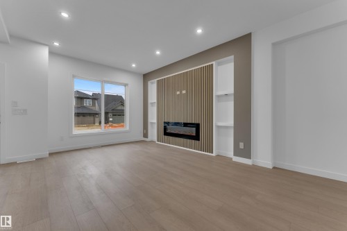 Spacious room with wood-finish flooring, recessed lighting, and a prominent media wall featuring a built-in fireplace and integrated shelving - 265 Falcon Crescent, Leduc, AB 