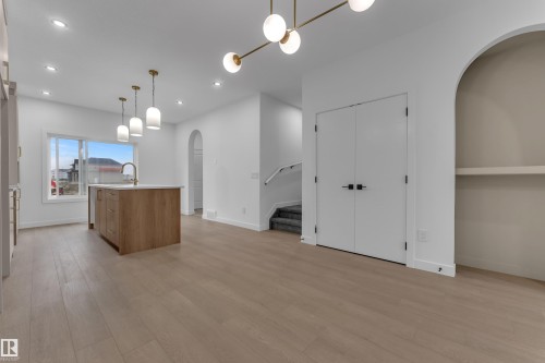 Open-concept living space featuring wood-finish flooring, a kitchen island with pendant lighting, recessed ceiling lights, and an arched entry - 265 Falcon Crescent, Leduc, AB 