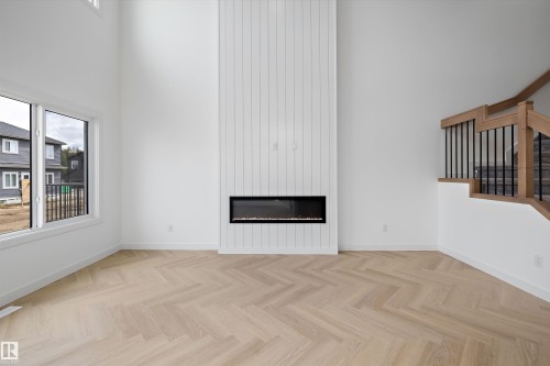 Herringbone wood-finish flooring, two-story ceiling, linear electric fireplace with shiplap surround, and a staircase with wood newel posts and metal spindles - Edmonton, AB 