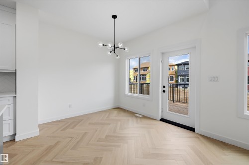 Light wood-finish flooring with a herringbone pattern, contemporary chandelier, white walls, and a glass-paneled door - Edmonton, AB 