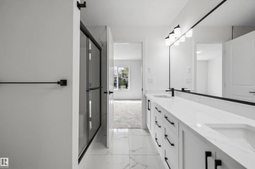 Dual vanity with integrated sinks, expansive wall-mounted mirror, modern black fixtures, and a glass-enclosed shower - Edmonton, AB 