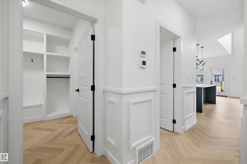 Herringbone wood-finish flooring, wainscoting detailing, built-in shelving, white paneled doors with matte black hardware, and integrated wall controls - Edmonton, AB 