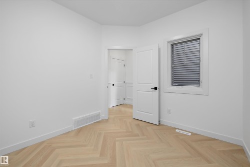 Herringbone wood-finish flooring, white trim, solid core doors with matte black hardware, and a window with horizontal blinds - Edmonton, AB 