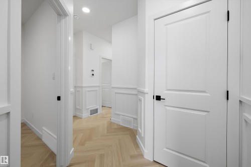 Herringbone wood-finish flooring, recessed lighting, white paneled doors with matte black hardware, and wainscoting with decorative trim - Edmonton, AB 