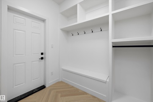 Entryway featuring built-in shelving, seating bench, coat hooks, and wood-finish herringbone flooring - Edmonton, AB 