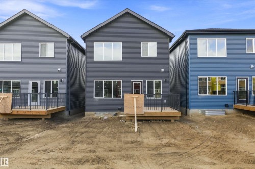 Rear exterior featuring dark gray horizontal siding, multiple windows, a ground-level wood-finish deck with black metal railing, and an exterior door with glass insert - Edmonton, AB 