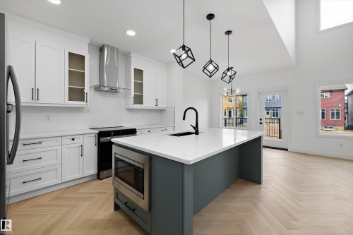 Kitchen featuring white cabinetry, a built-in microwave, a central island with a white countertop, and wood-finish herringbone flooring - Edmonton, AB 