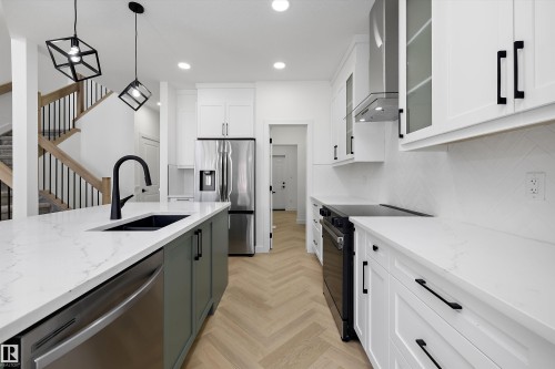 Kitchen featuring a center island with sink, stainless steel appliances, white cabinetry with black hardware, and wood-finish flooring in a herringbone pattern - Edmonton, AB 