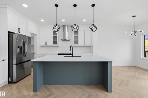 Modern kitchen featuring an island with a quartz countertop, stainless steel appliances, white cabinetry, and herringbone wood-finish flooring - Edmonton, AB 