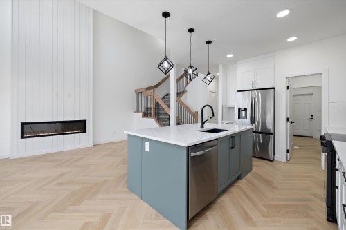 Herringbone wood-finish flooring, two-story vertical shiplap accent wall, built-in linear fireplace, kitchen island with integrated sink, and stainless steel appliances - Edmonton, AB 