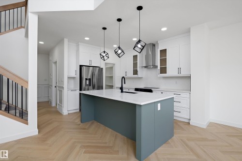 Open-concept kitchen featuring a large island, white cabinetry, stainless steel appliances, and wood-finish flooring in a herringbone pattern - Edmonton, AB 