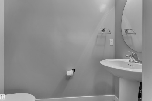 Pedestal sink with chrome faucet, complemented by a round wall-mounted mirror - 12221 117 Avenue Nw, Edmonton, AB - Indoor Photo Showing Bathroom