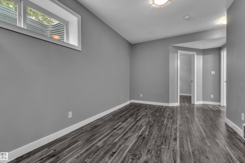 Spacious room featuring wood-finish flooring, light grey painted walls, white baseboards, and a window with a window well - 12221 117 Avenue Nw, Edmonton, AB - Indoor Photo Showing Other Room