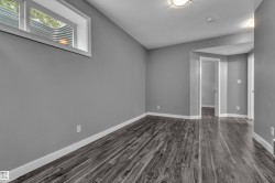 Spacious room featuring wood-finish flooring, light grey painted walls, white baseboards, and a window with a window well - 