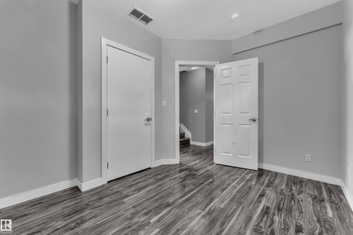 Room featuring wood-finish flooring, light gray walls, white baseboards, and two white doors - 12221 117 Avenue Nw, Edmonton, AB - Indoor Photo Showing Other Room