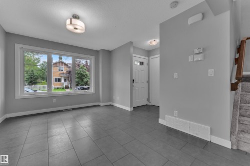 Spacious entry area featuring large format tile flooring, a prominent three-panel window, a white paneled entry door with frosted glass inserts, and a carpeted staircase with a wood handrail - 12221 117 Avenue Nw, Edmonton, AB - Indoor Photo Showing Other Room