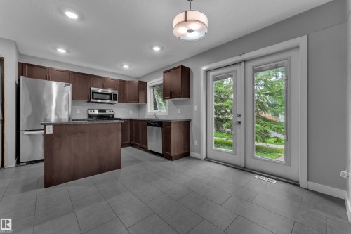 Contemporary kitchen featuring dark wood-finish cabinetry, stainless steel appliances, and a central island with a contrasting countertop - 12221 117 Avenue Nw, Edmonton, AB - Indoor Photo Showing Kitchen