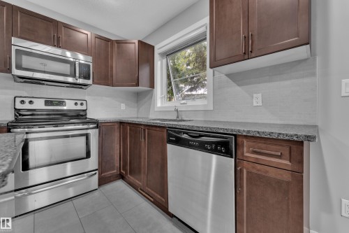Kitchen featuring stainless steel appliances, dark wood cabinetry, light tile backsplash, gray countertop, and tile flooring - 12221 117 Avenue Nw, Edmonton, AB - Indoor Photo Showing Kitchen