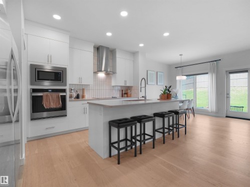 Modern kitchen featuring white cabinetry, stainless steel appliances, a center island with bar seating, and wood-finish flooring - 22650 99A Avenue Nw, Edmonton, AB - Indoor Photo Showing Kitchen With Upgraded Kitchen