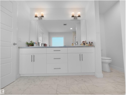 Dual vanity with white cabinetry, integrated sinks, a generous mirror, and overhead lighting fixtures - 22650 99A Avenue Nw, Edmonton, AB - Indoor Photo Showing Bathroom