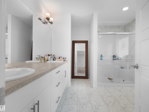 Bathroom featuring a spacious double vanity with white cabinetry and integrated sinks, a large mirror, and a glass-enclosed shower with tile surround - 22650 99A Avenue Nw, Edmonton, AB - Indoor Photo Showing Bathroom