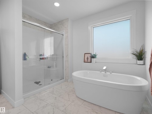 Contemporary bathroom featuring a freestanding soaking tub with deck-mounted chrome fixtures, a spacious walk-in shower with clear glass doors and tiled surround, a large window with white trim, and light-toned tile flooring - 22650 99A Avenue Nw, Edmonton, AB - Indoor Photo Showing Bathroom