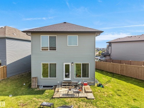 Rear exterior featuring light gray horizontal siding, multiple windows, a ground-level door, and a wooden deck - 22650 99A Avenue Nw, Edmonton, AB - Outdoor With Exterior